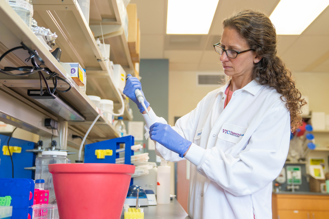 Lab setting with a female researcher injecting fluid into a container. 